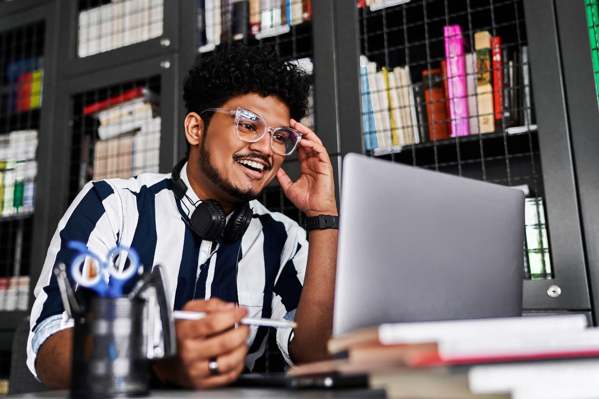 Young, stylish man with curly hair and clear framed glasses working on a laptop