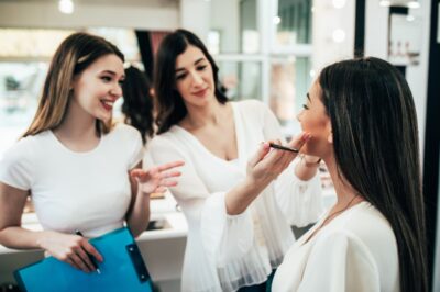 Three white woman with white shirts teaching and learning makeup application techniques in a salon