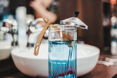 Straight razor and comb inside glass container with blue sanitation liquid at salon or barber shop