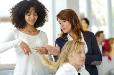 Cosmetology instructor teaching stylist student how to cut hair